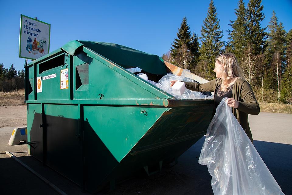 En kvinna som sorterar plast i en container på en återvinningscentral. 