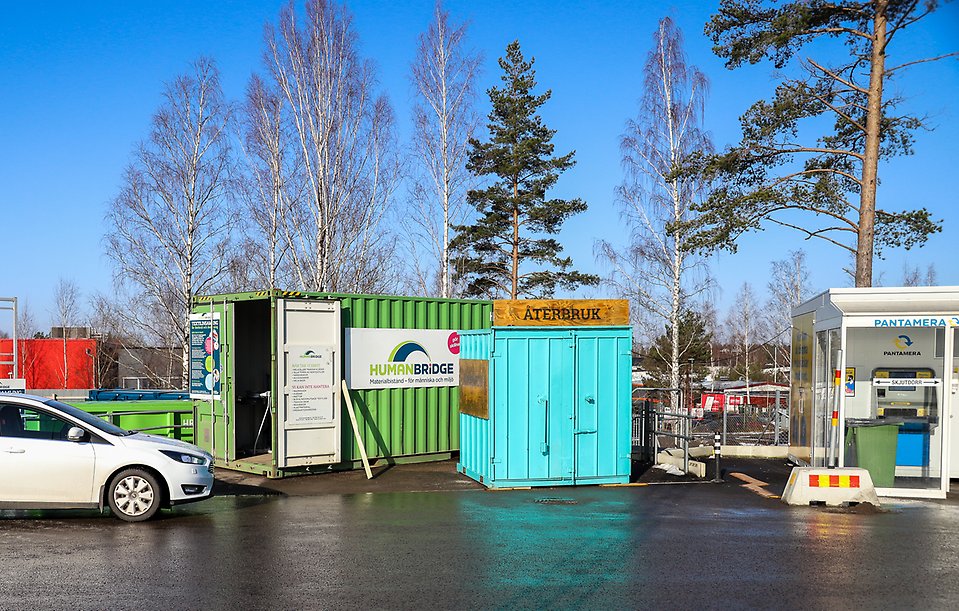 En stor grön metallcontainer för textilinsamling bredvid en mindre turkos container.
