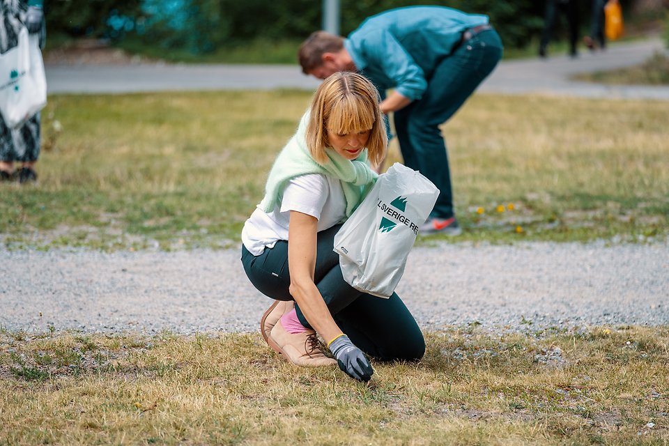 Kvinna plockar skräp från en gräsmatta under Håll Sverige rent-dagen.